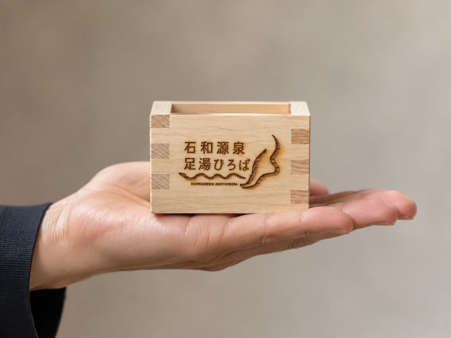 ロゴを刻んだ一合枡を手のひらに載せたサイズ感